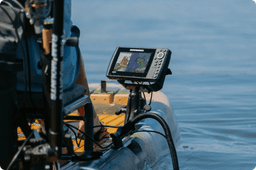 Close-up of a mounted Humminbird fish finder attached to a camo kayak, positioned beside a paddle and various gear.